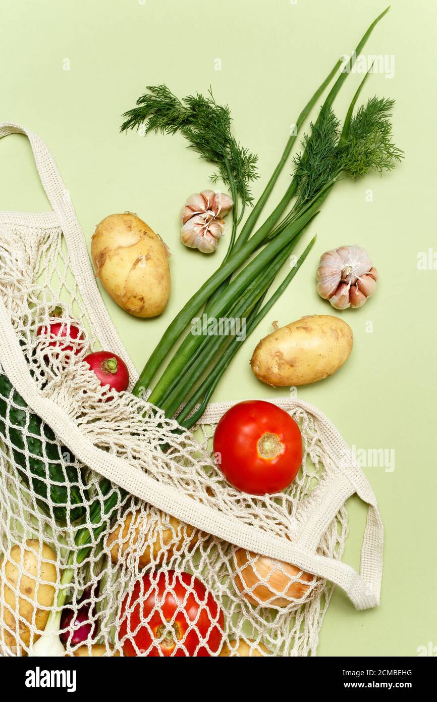 Trendige Saitenbeutel mit frischem Gemüse und Gemüse auf hellgrünem Hintergrund: Kartoffeln, Tomaten, Zwiebeln, Knoblauch. Zero Waste nachhaltiger Lebensstil CO Stockfoto