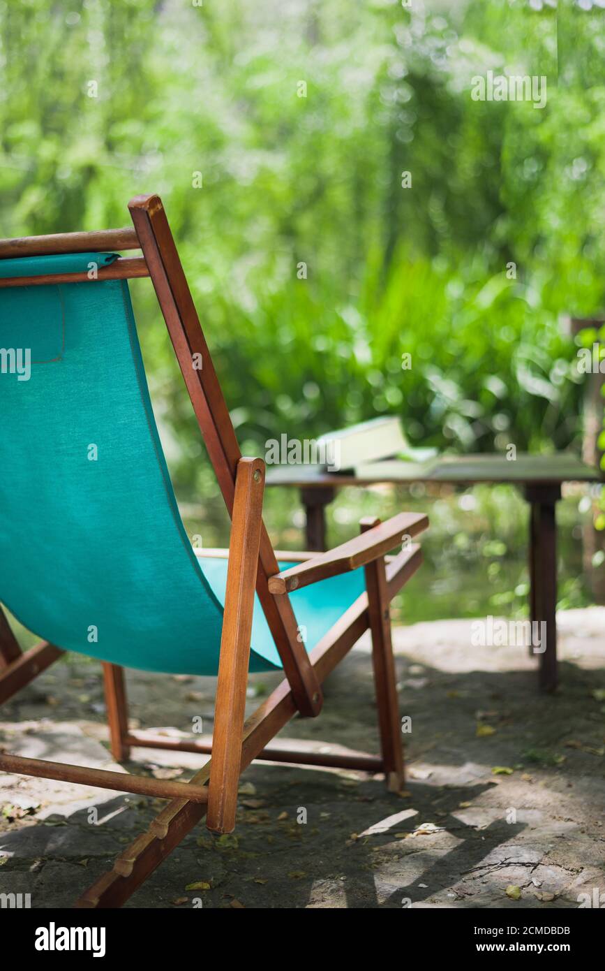 Vertikales Farbbild mit einer Seitenansicht eines hölzernen Strandstuhls im Garten und einigen Büchern im Garten. Entspannendes Hotel-Konzept. Stockfoto