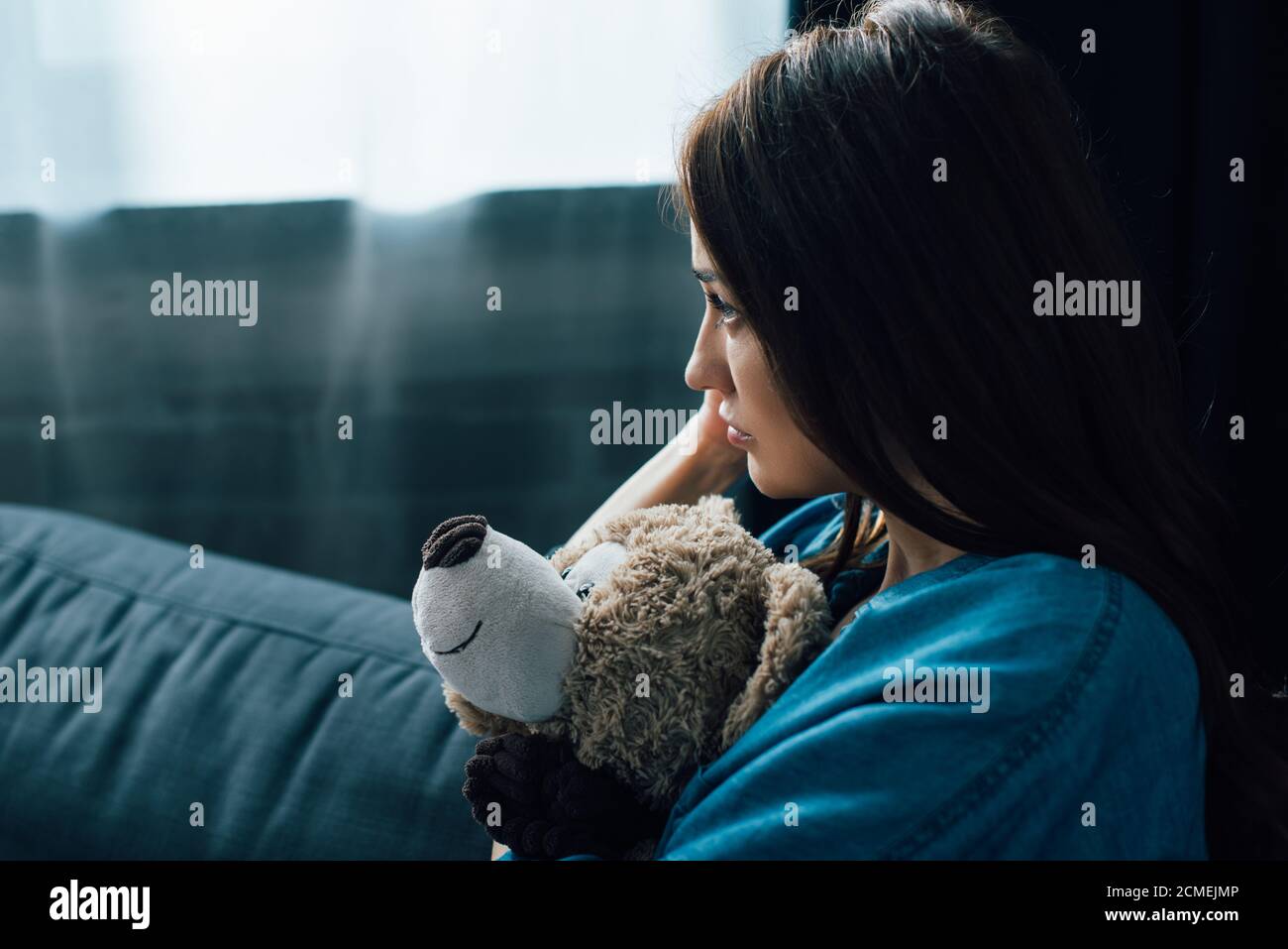 Deprimierte Brünette Frau hält Teddybär beim Blick weg Stockfoto