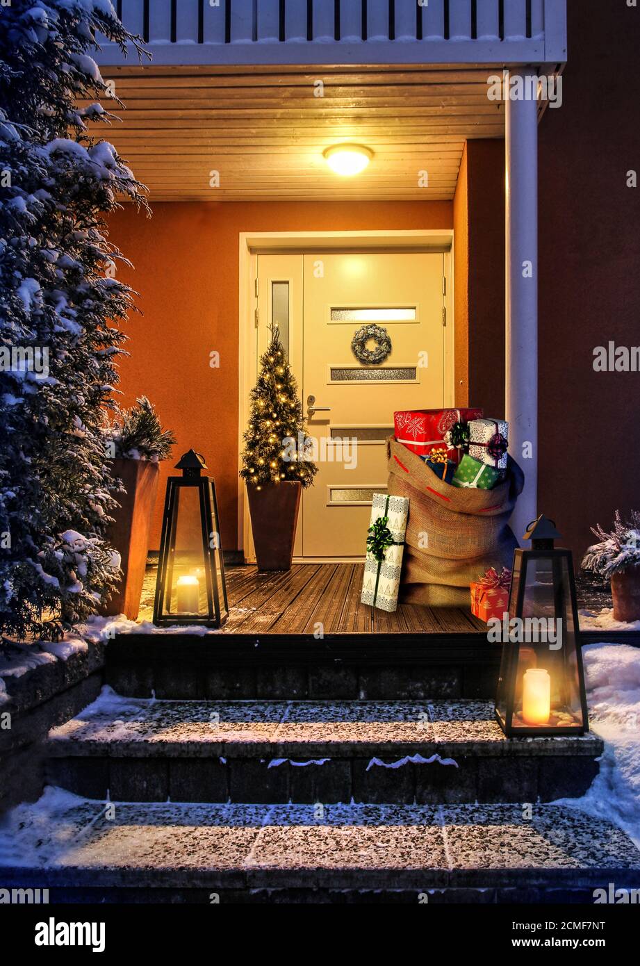 Willkommen Weihnachten - Haus Eingang verschneiten Treppen und Tür mit Dekoration. Santas Geschenksack mit Geschenkschachteln Stockfoto