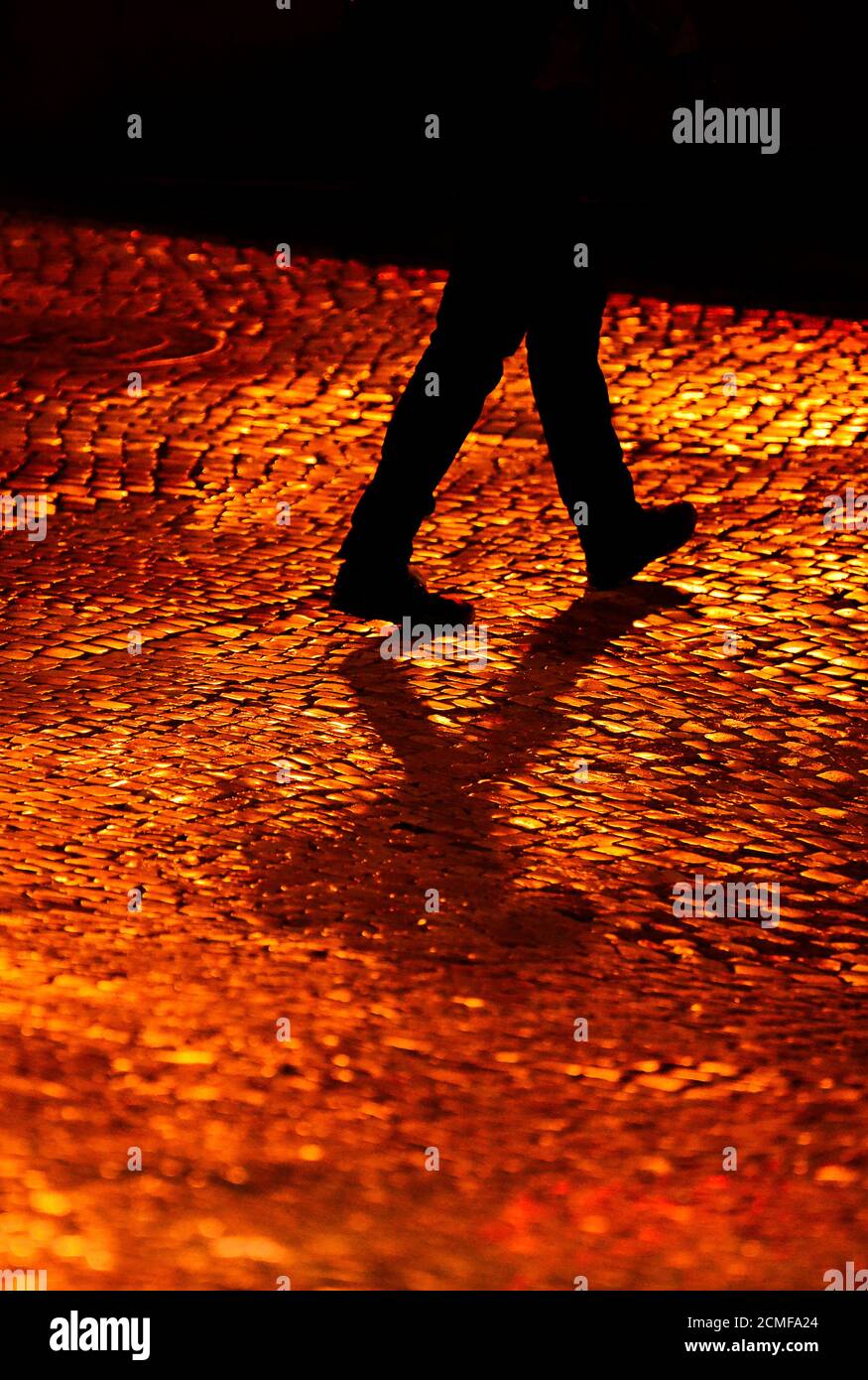 Mann, der auf Kopfsteinpflaster läuft, beleuchtet von warmen Straßenlaternen Nacht Stockfoto