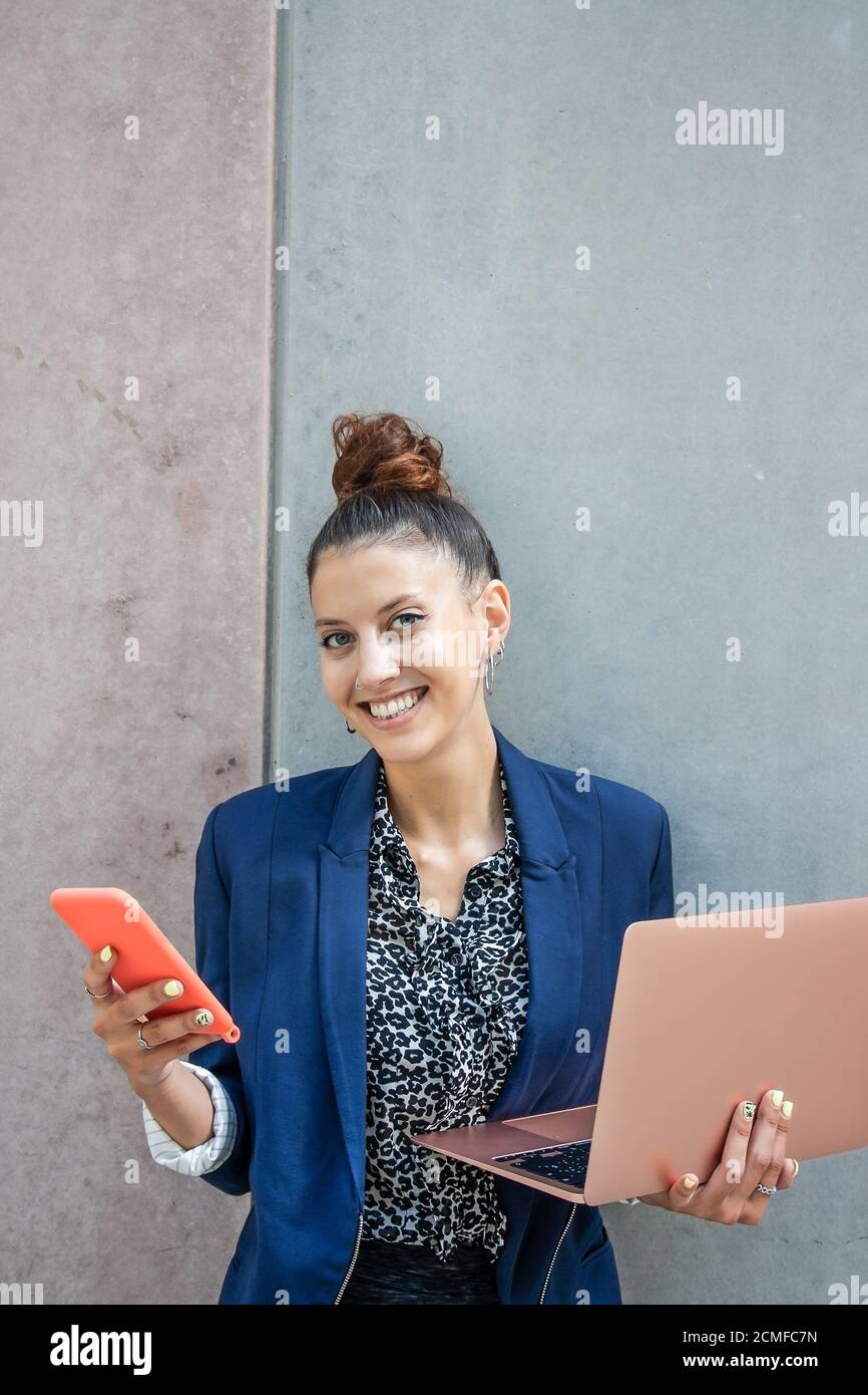 Junge Geschäftsfrau Porträt mit ihren digitalen Werkzeugen in der Hand. Handy und Computer. Mittlere Nahaufnahme. Horizontale Ansicht. Stockfoto