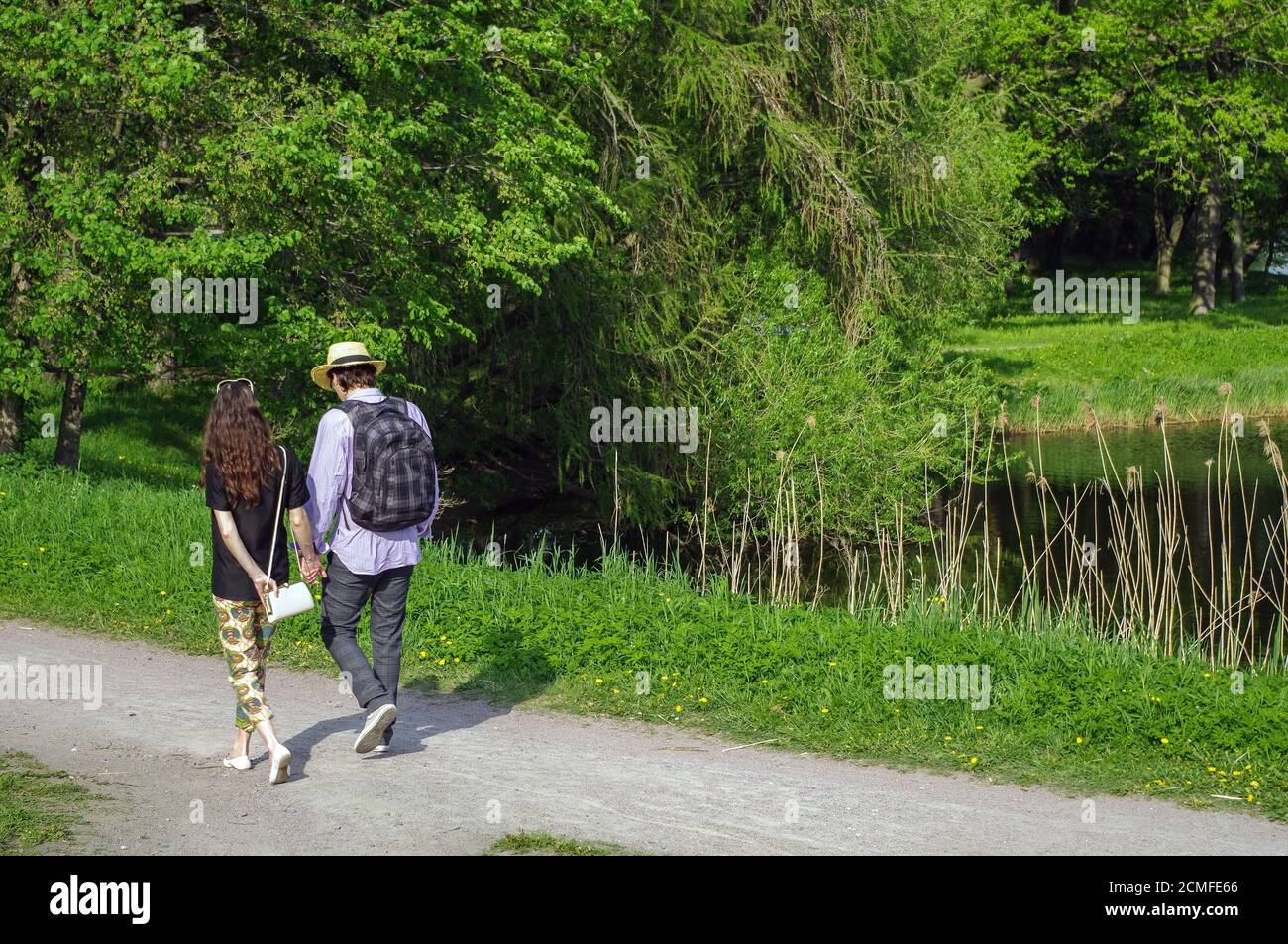 Glückliches junges Paar, das im Sommerpark mit Händen läuft Ein Teich an der Seite Stockfoto