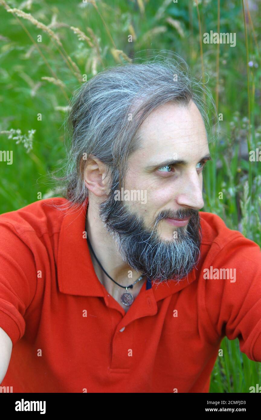 Junge bärtige Mann sitzt drausen auf sonnigen Tag mit grünem Hintergrund. Dies ist ein Porträt Stockfoto
