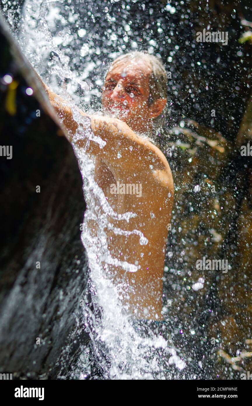 Mann, der eine entspannende Dusche unter einem Wasserfall. außerhalb Stockfoto