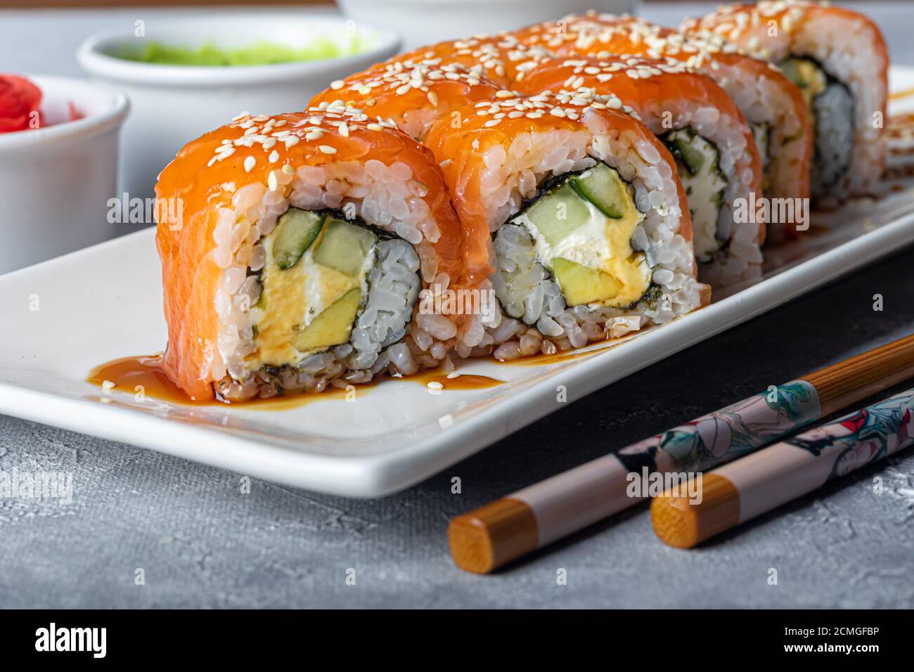 Sushi setzt Nigiri, Uramaki, California, Philadelphia, auf einen weißen Teller. In der Nähe Ingwer und Wasabi. Sojasauce in einer weißen Schüssel. Auf hellgrauem Hintergrund Stockfoto