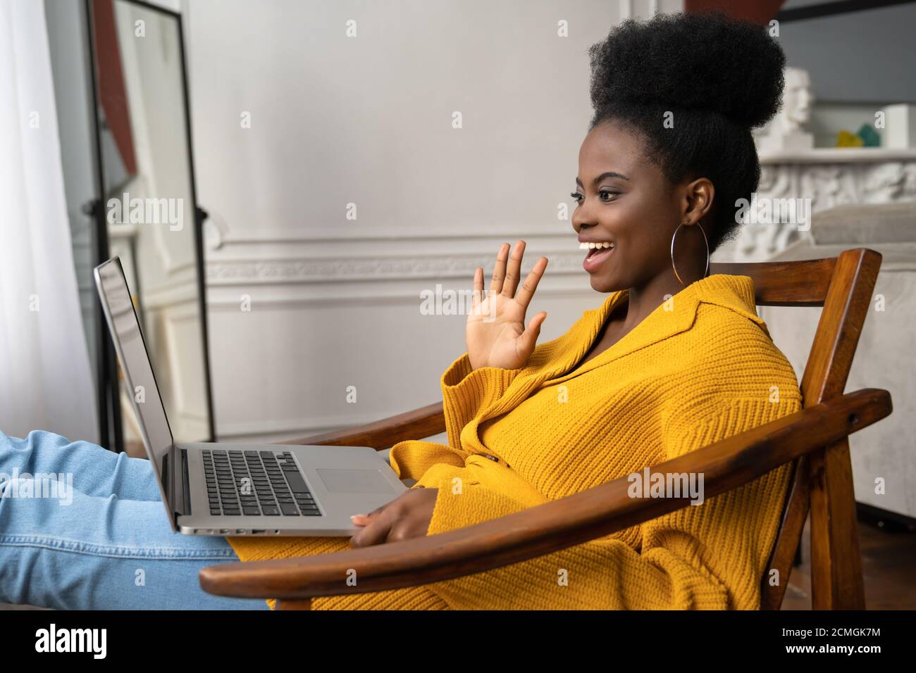 Lächelnde afroamerikanische Biracial Millennial Frau mit Afro-Frisur in gelber Strickjacke ruhen, sitzen auf Sessel, im Video-Chat mit ihr zu sprechen Stockfoto
