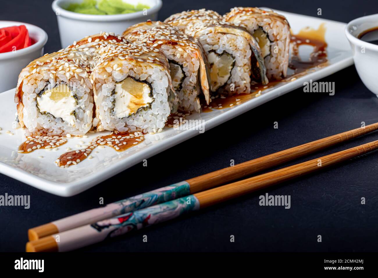 Sushi setzt Uramaki, California, Philadelphia, auf einen weißen Teller. In der Nähe Ingwer und Wasabi. Sojasauce in einer weißen Schüssel. Auf einem dunklen Hintergrund. Speicherplatz kopieren. Stockfoto