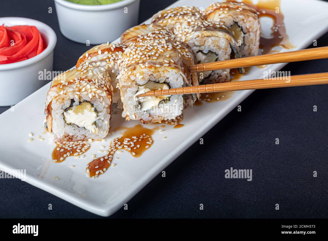 Sushi setzt Uramaki, California, Philadelphia, auf einen weißen Teller. In der Nähe Ingwer und Wasabi. Sojasauce in einer weißen Schüssel. Auf einem dunklen Hintergrund. Speicherplatz kopieren. Stockfoto
