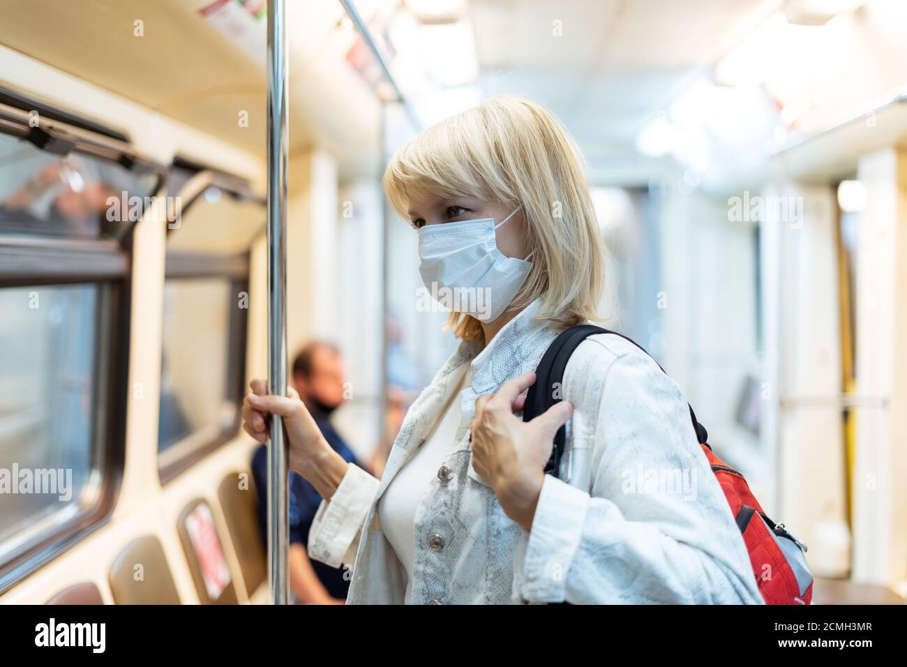 Portrait der schönen erwachsenen Frau in medizinischer Schutzmaske mit Rucksack steht in der U-Bahn und blickt nach vorne. Stockfoto