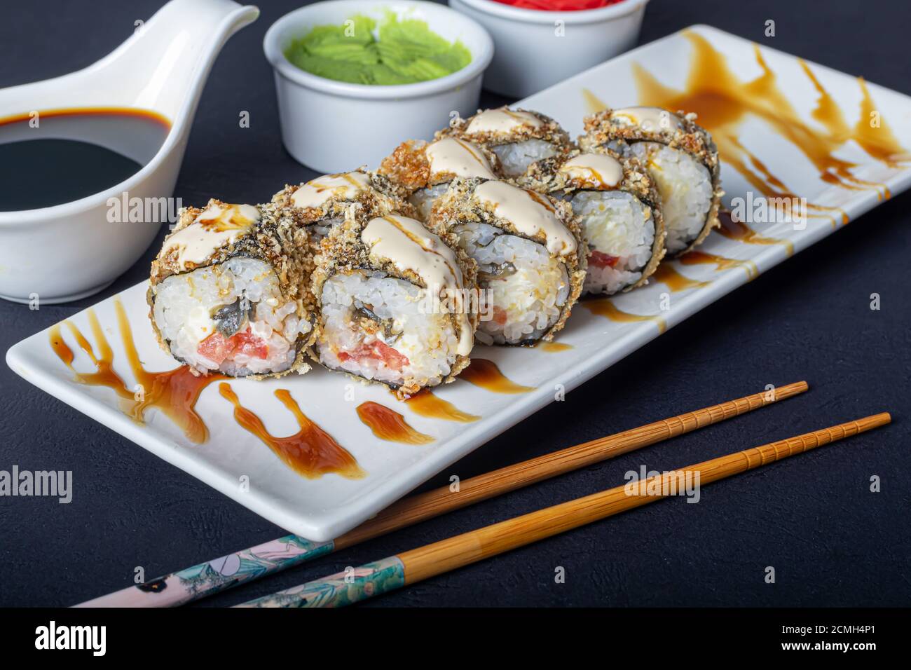 Sushi setzt Uramaki, California, Philadelphia, auf einen weißen Teller. In der Nähe Ingwer und Wasabi. Sojasauce in einer weißen Schüssel. Auf einem dunklen Hintergrund. Speicherplatz kopieren. Stockfoto