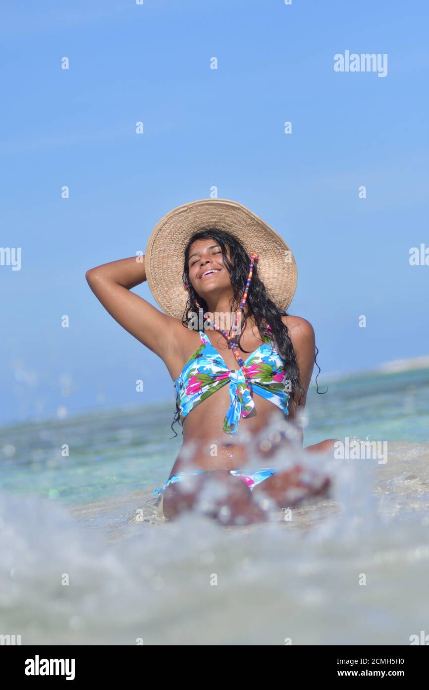 Hispanische Frau sitzt am Sandstrand und lacht mit geschlossenen Augen und Spritzwasser. Los Roques Venezuela Stockfoto