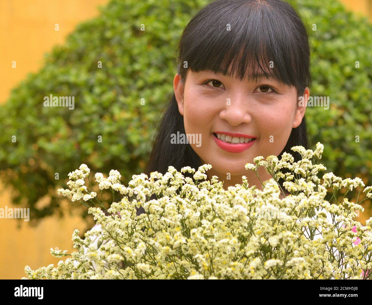 Schöne junge vietnamesische weibliche Floristin zeigt einen Blumenstrauß von Statice Creme Blumen und lächelt für die Kamera. Stockfoto