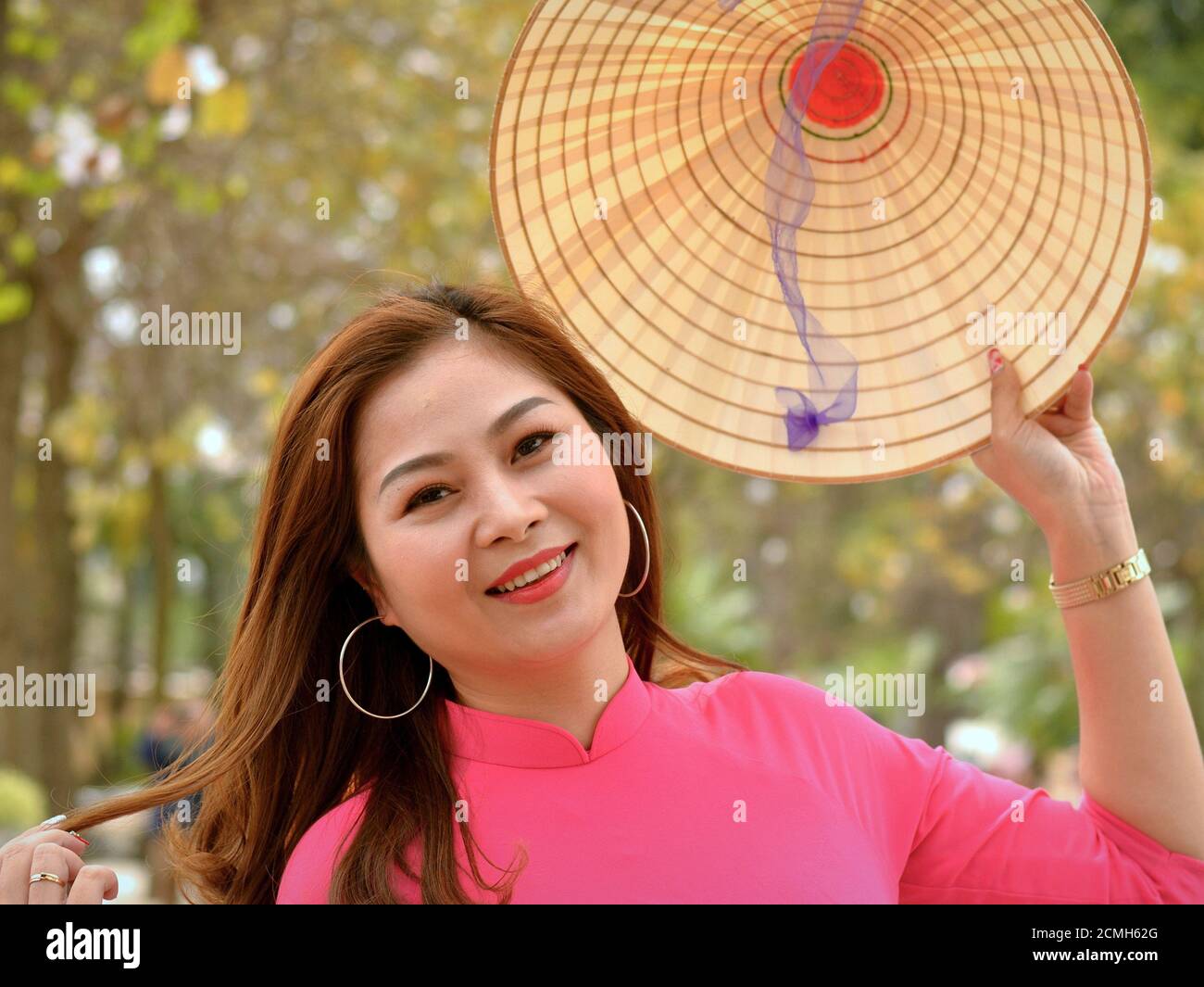 Schöne junge lächelnde vietnamesische Frau hält einen traditionellen asiatischen konischen Strohhut mit ihrer linken Hand und Posen für die Kamera. Stockfoto
