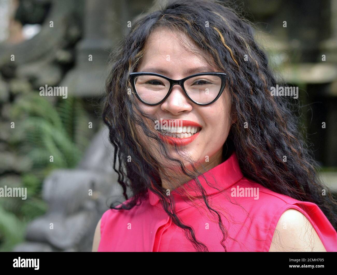 Junge attraktive fröhliche vietnamesische Frau mit großen Brillen trägt eine rosa Bluse und lächelt für die Kamera. Stockfoto