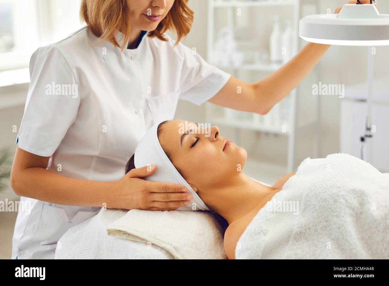 Kosmetikerin oder Dermatologin, die Lampe zum Gesicht der Frau leitet Behandlung Stockfoto