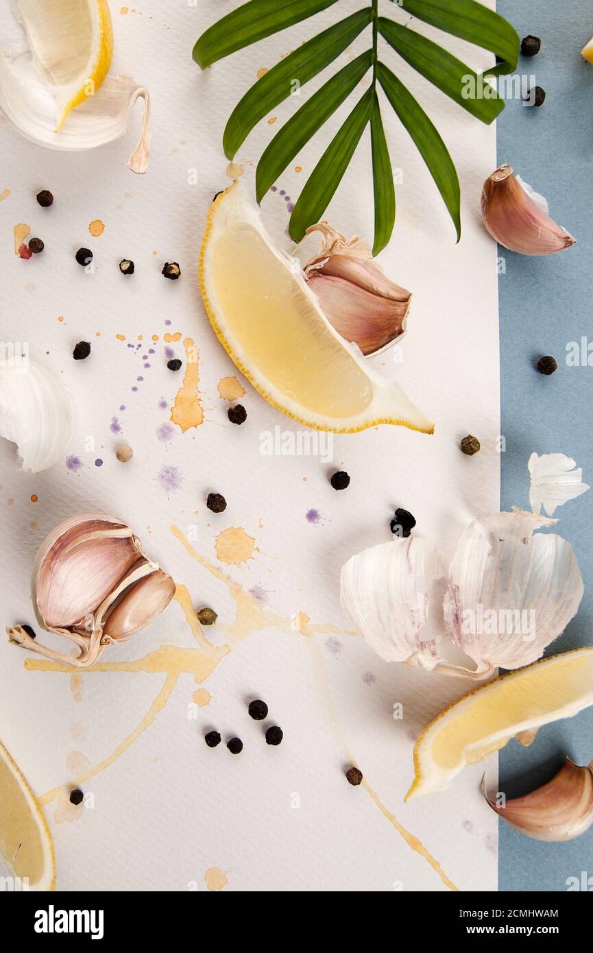 Knoblauchzehen, schwarzer Pfeffer und Zitronenscheiben sind auf weißem Hintergrund mit Aquarellsprays. Stockfoto