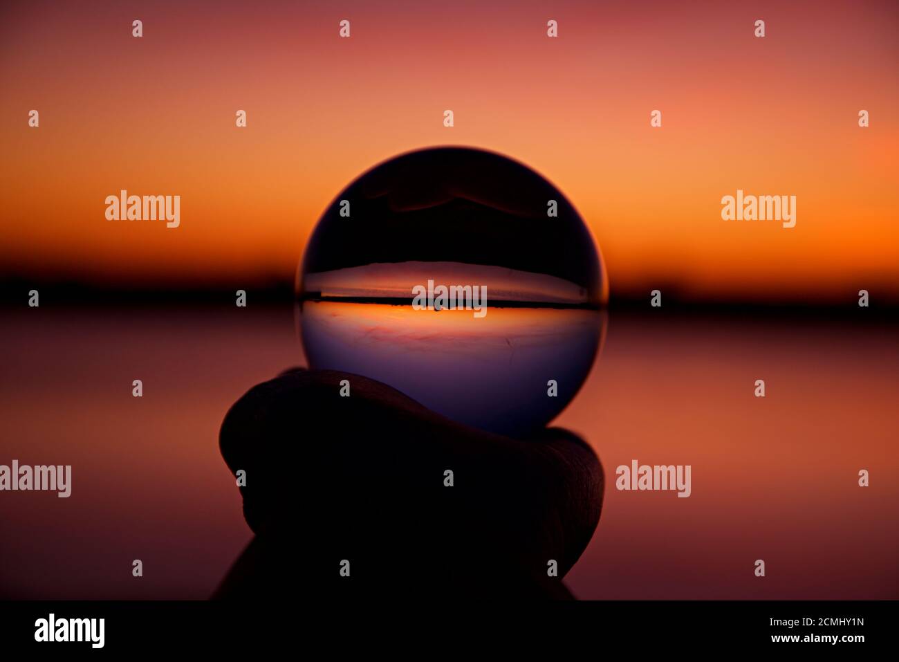 Sonnenuntergang über Assateague Island über Sümpfen, Salzwasserbucht in Kristallkugel von einer Hand gehalten reflektiert. Stockfoto