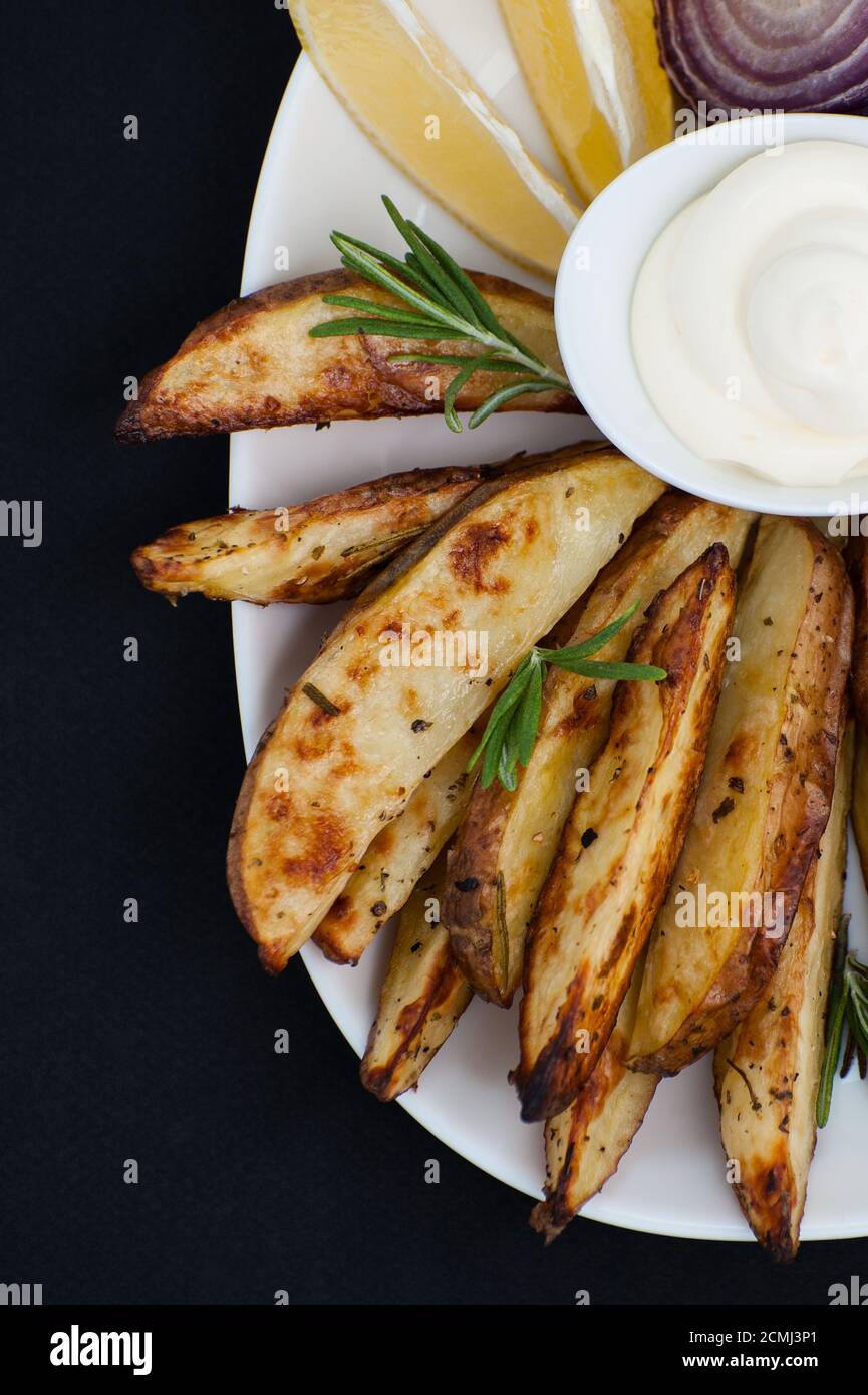 Gebackene Kartoffeln mit Rosmarin und Aioli-Sauce auf schwarzem Hintergrund. Stockfoto