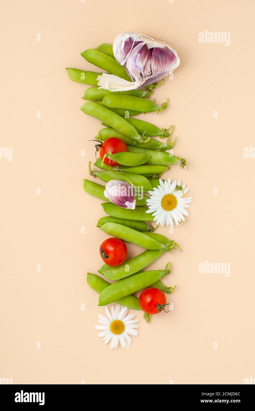 Junge grüne Erbsen, Knoblauch, Tomaten und Blumen Gänseblümchen auf der rechten Seite auf einem hellgelben Pastell-Backgro Stockfoto