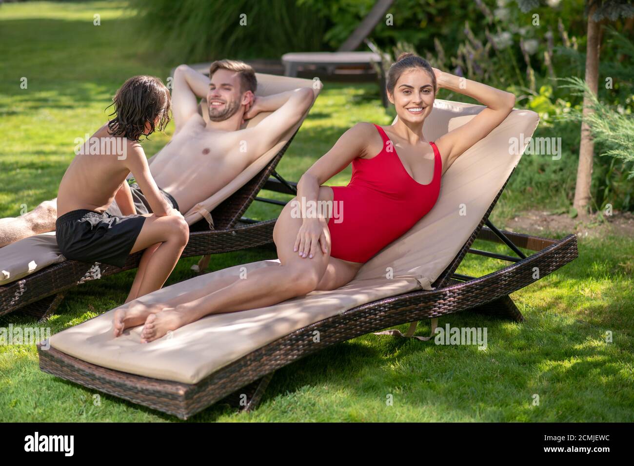 Schöne Frau in roten Badeanzug Mann und Junge hinter Stockfoto