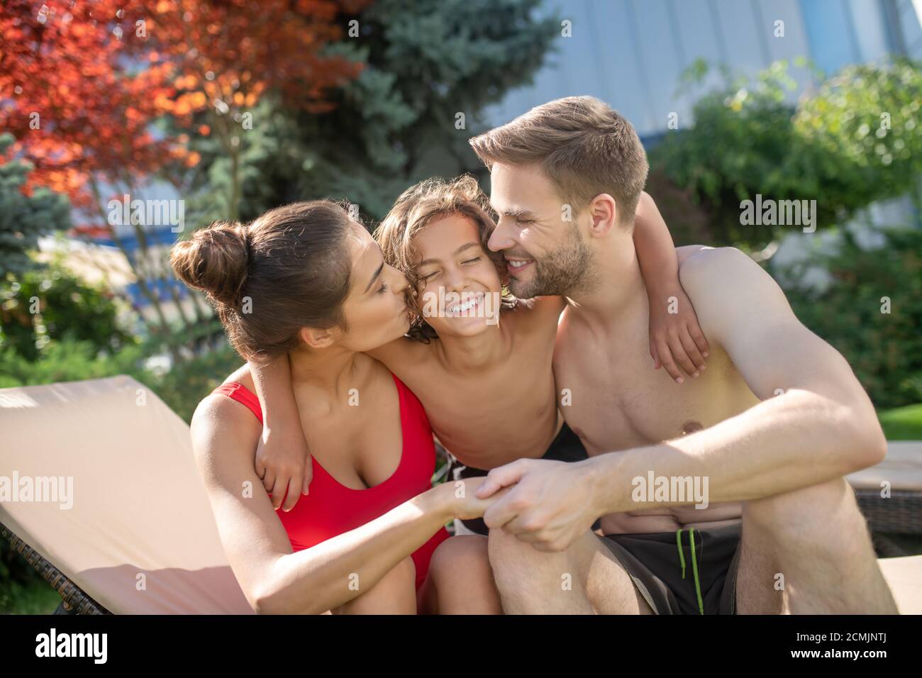 Liebevolle Eltern, die ihren Sohn umarmten und ihn küssen Stockfoto