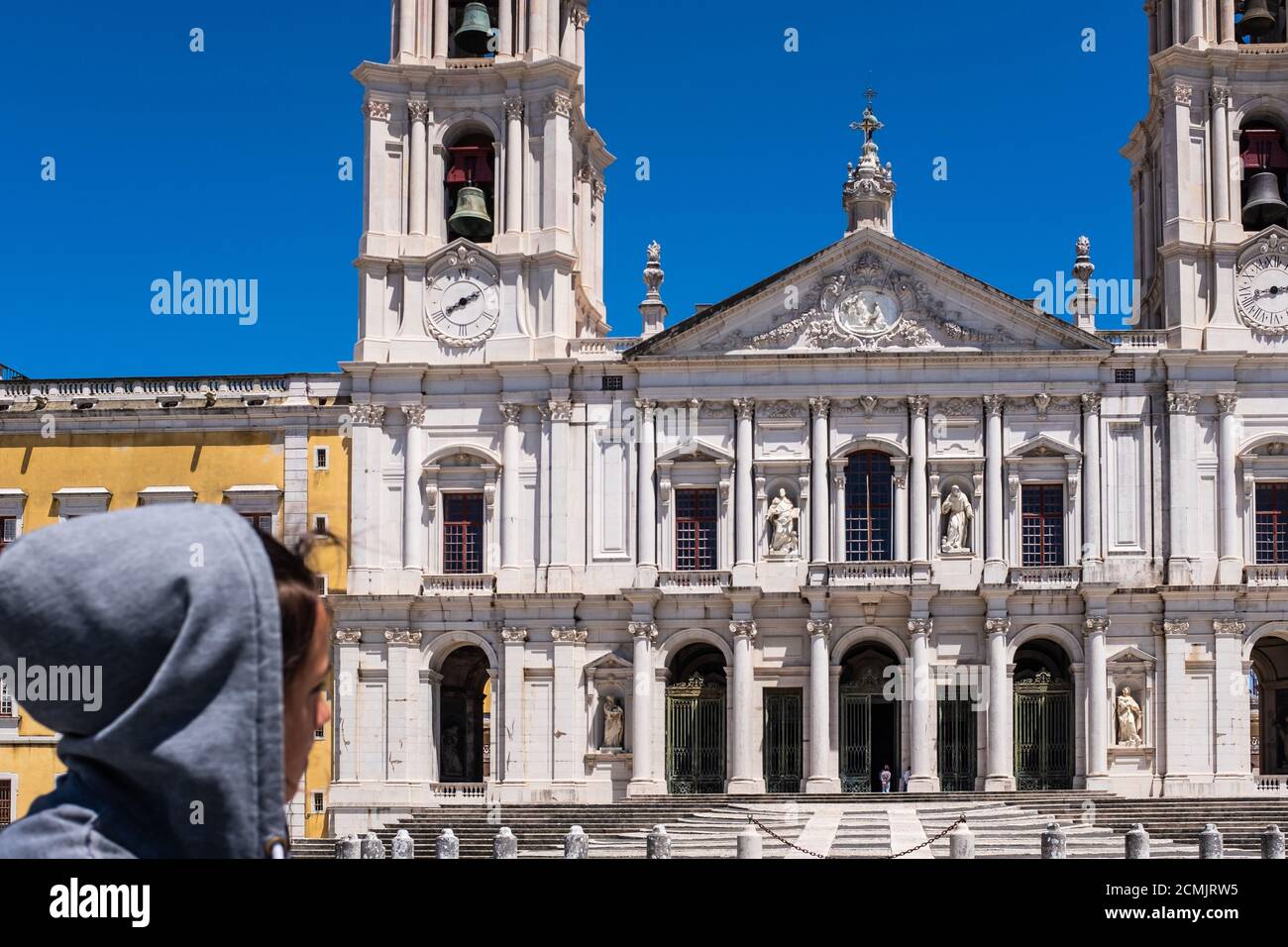 Profil verschwommen von einem Teenager-Mädchen in einem grauen Hoodie und Blick auf die façade der Basilika im Mafra National Palace (Portugal). Stockfoto