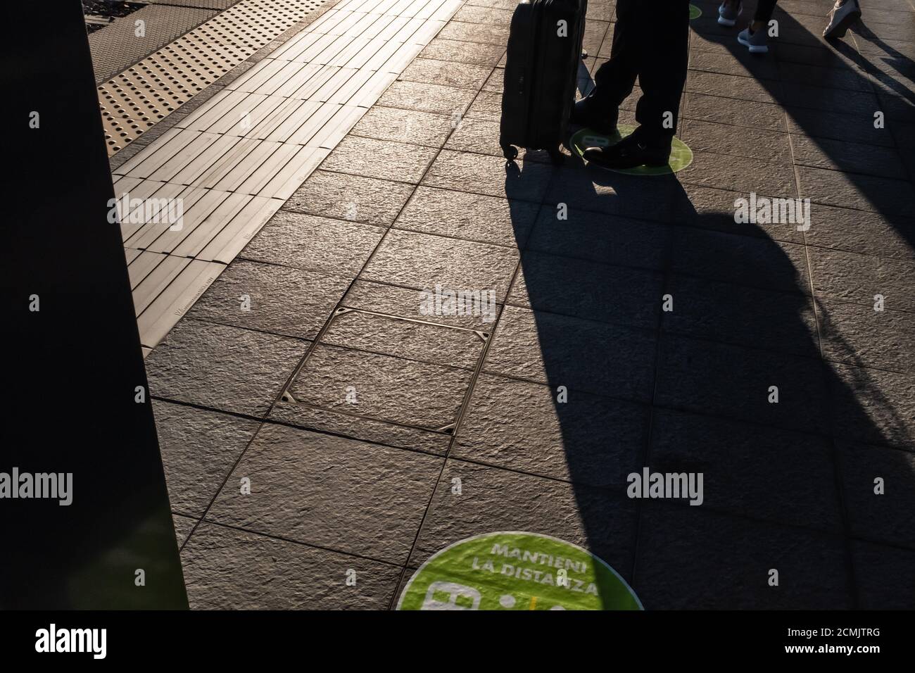 Silhouette Reisender Mann stehend mit Gepäck wartet auf den Zug. „Halten Sie Abstand“ ist der Text der grünen Grafiken, die auf den Boden geklebt sind Stockfoto