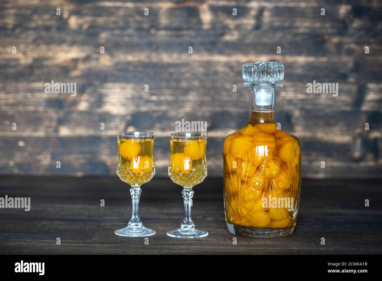 Hausgemachte Tinktur aus gelber Kirsche Pflaume in einer Kristallflasche und ein zwei Wein Kristallglas auf Holzhintergrund, Ukraine, Nahaufnahme. Beerenalkoholisches drin Stockfoto