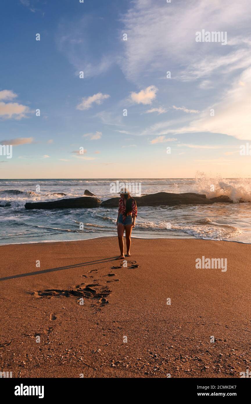 Eine junge Frau, die durch Wellen am Strand steht Stockfoto