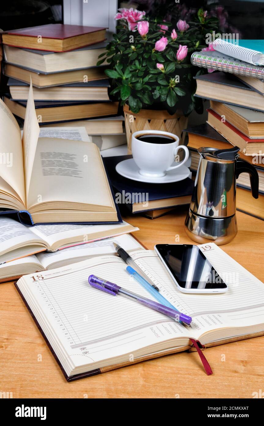 Lehrbücher, Notizblock und Stift mit einer Tasse schwarzen Kaffee mit einer Kaffeekanne auf einem Holztisch. Bildung Stockfoto