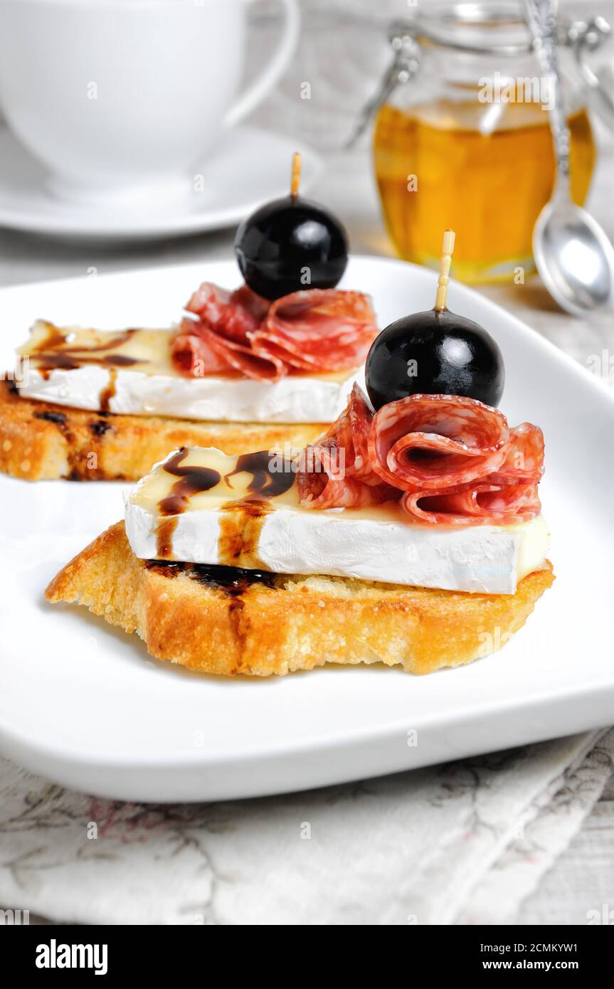 Snack aus einer gerösteten Scheibe Baguette mit weichen unter einem edlen weißen Schimmel Käse Brie, Salami, ein ber Stockfoto