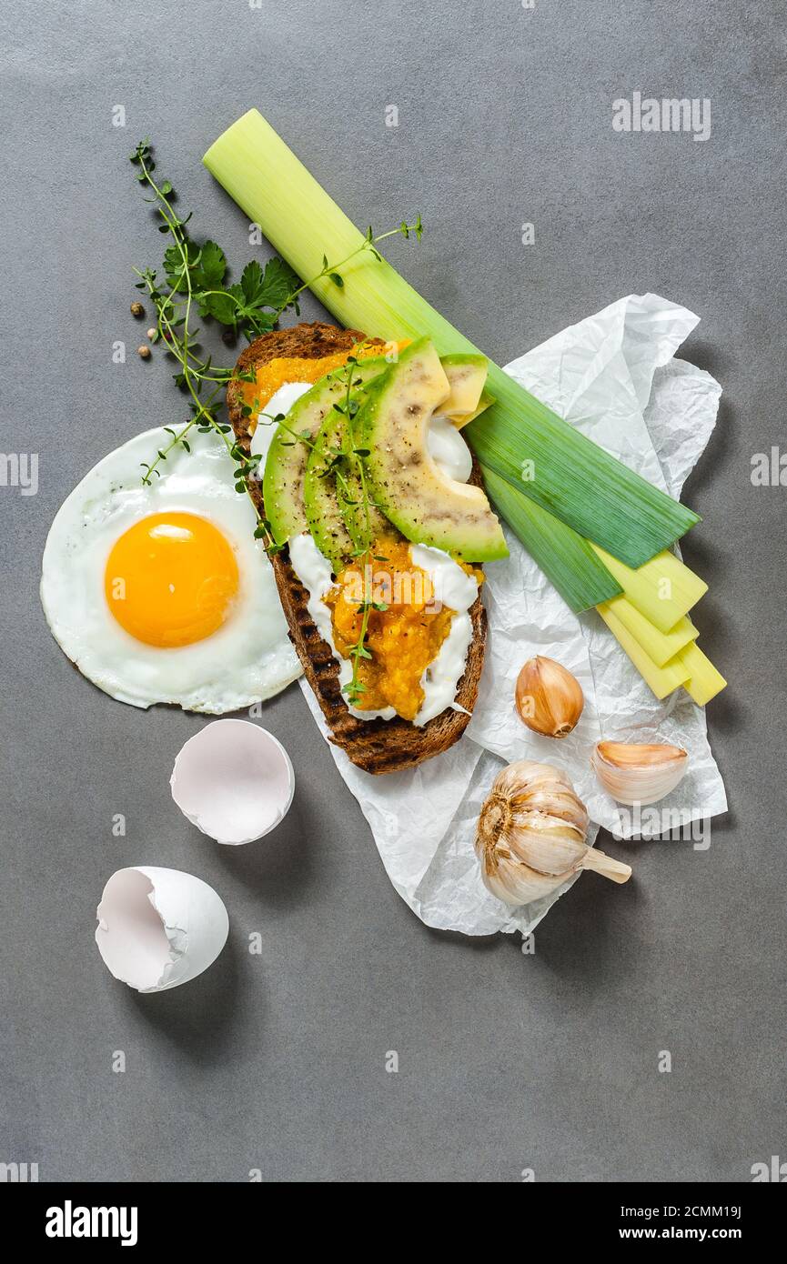 Sandwich mit Avocado, Paprikapaste und Spiegeleier auf einem grauen Steintisch. Stockfoto