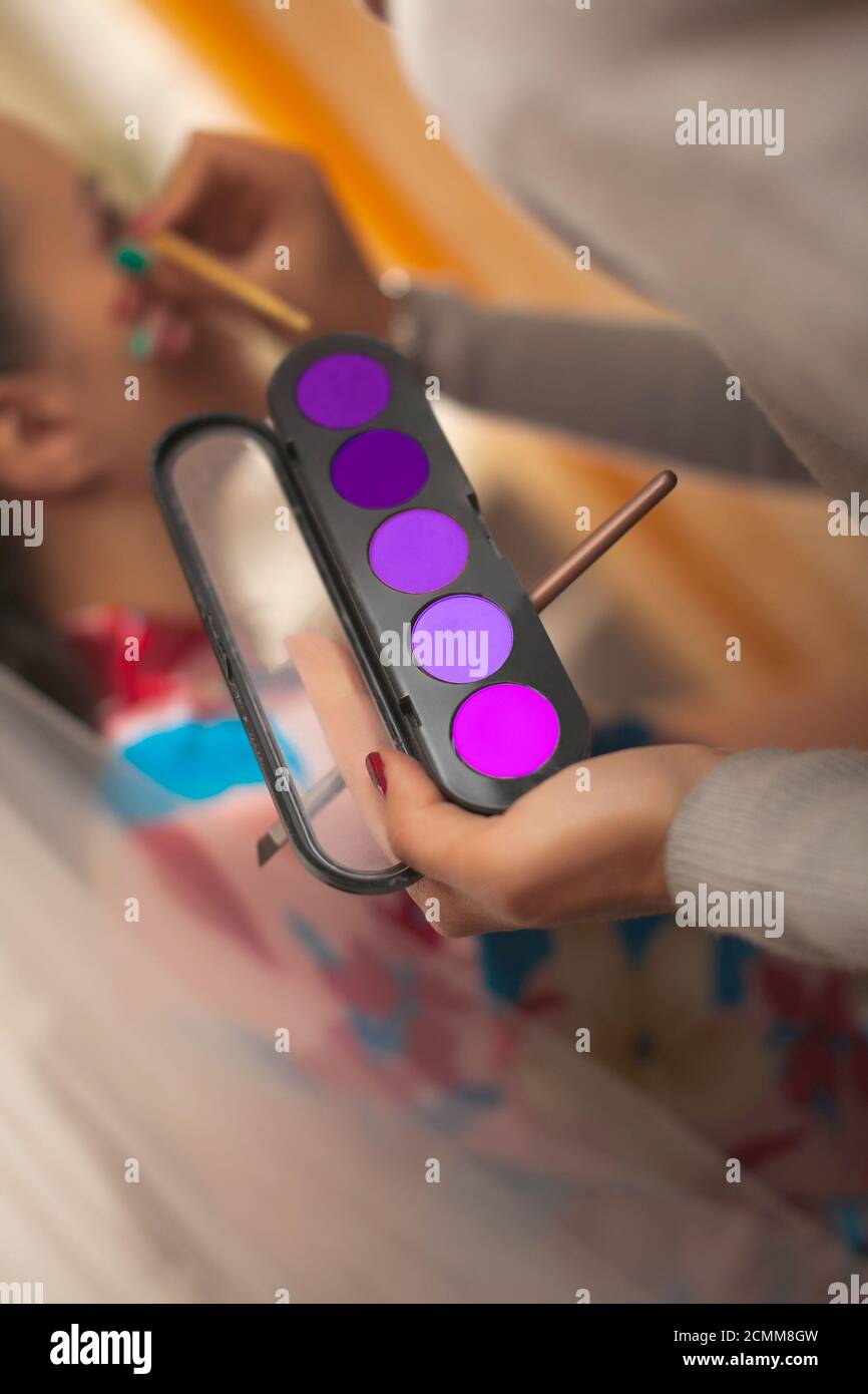Der Make-up-Künstler hält in seiner Hand ein Set Lidschatten im ultravioletten Bereich mit einem Pinsel Und Stockfoto