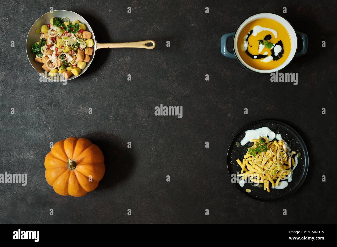 Orangefarbener Kürbis auf schwarzem Hintergrund mit Kürbisrezepten, Pasta, Gnocchi und Kürbissuppe, Herbstfrüchte mit leuchtenden Farben Stockfoto