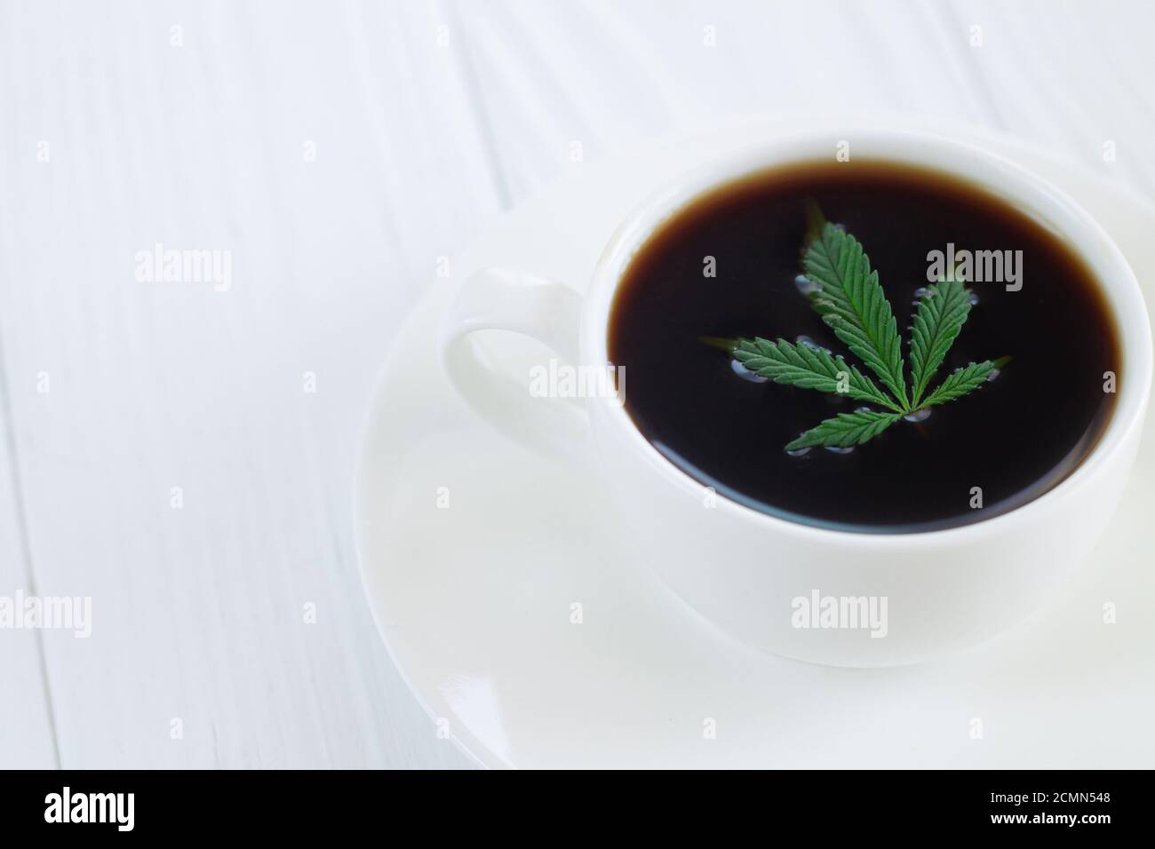 Weiße Tasse Cannabis-Kaffee mit Hanfblättern aus der Nähe Stockfoto