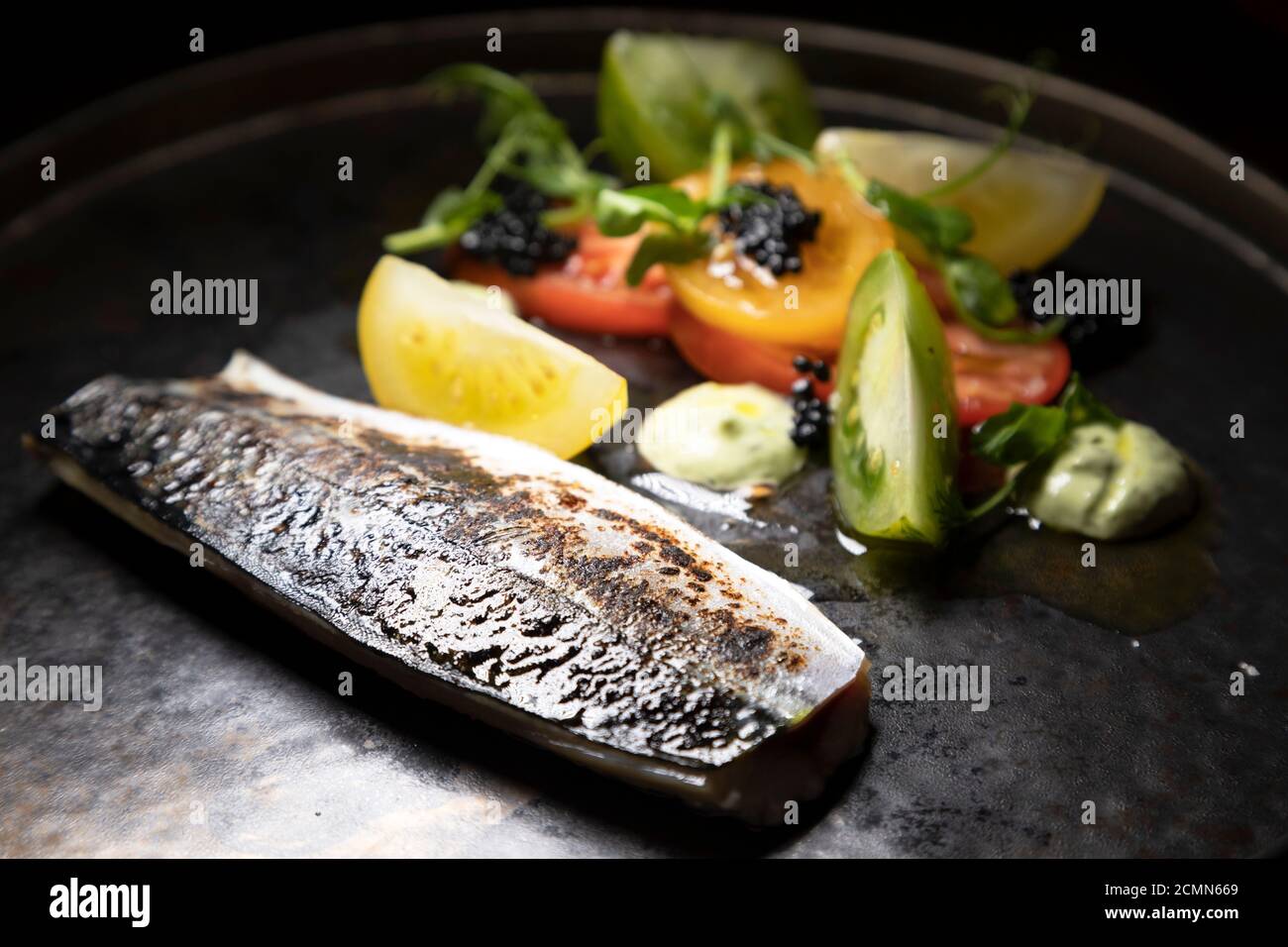 Makrele mit Kaviar serviert mit einem Salat mit Tomaten und Basilikum. Die Makrele wurde ausgehärtet und in Fackel gebracht. Stockfoto