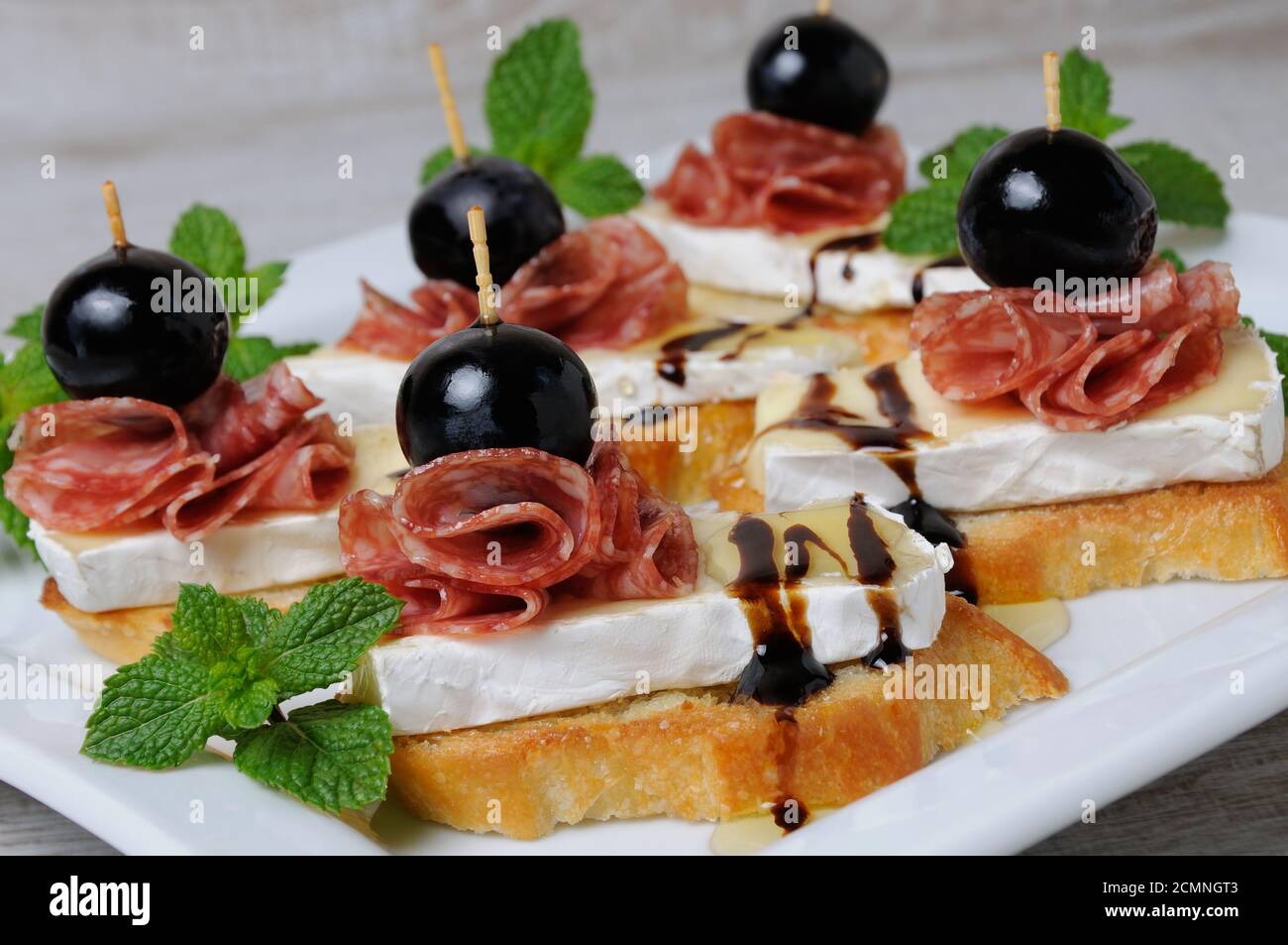 Snack aus einer gerösteten Scheibe Baguette mit weichen unter einem edlen weißen Schimmel Käse Brie, Salami, ein ber Stockfoto