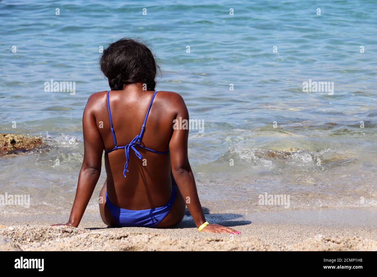 Schwarze Frau Sonnenbaden auf einem Sandstrand sitzen auf Wellen Hintergrund. Urlaub, Entspannung und Freizeit am Meer Stockfoto