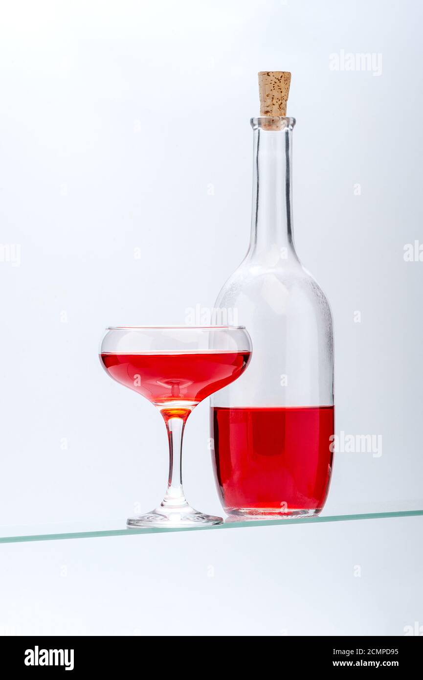 Weinglas und Flasche mit rotem Alkoholgetränk auf hellgrauem Hintergrund. Stockfoto