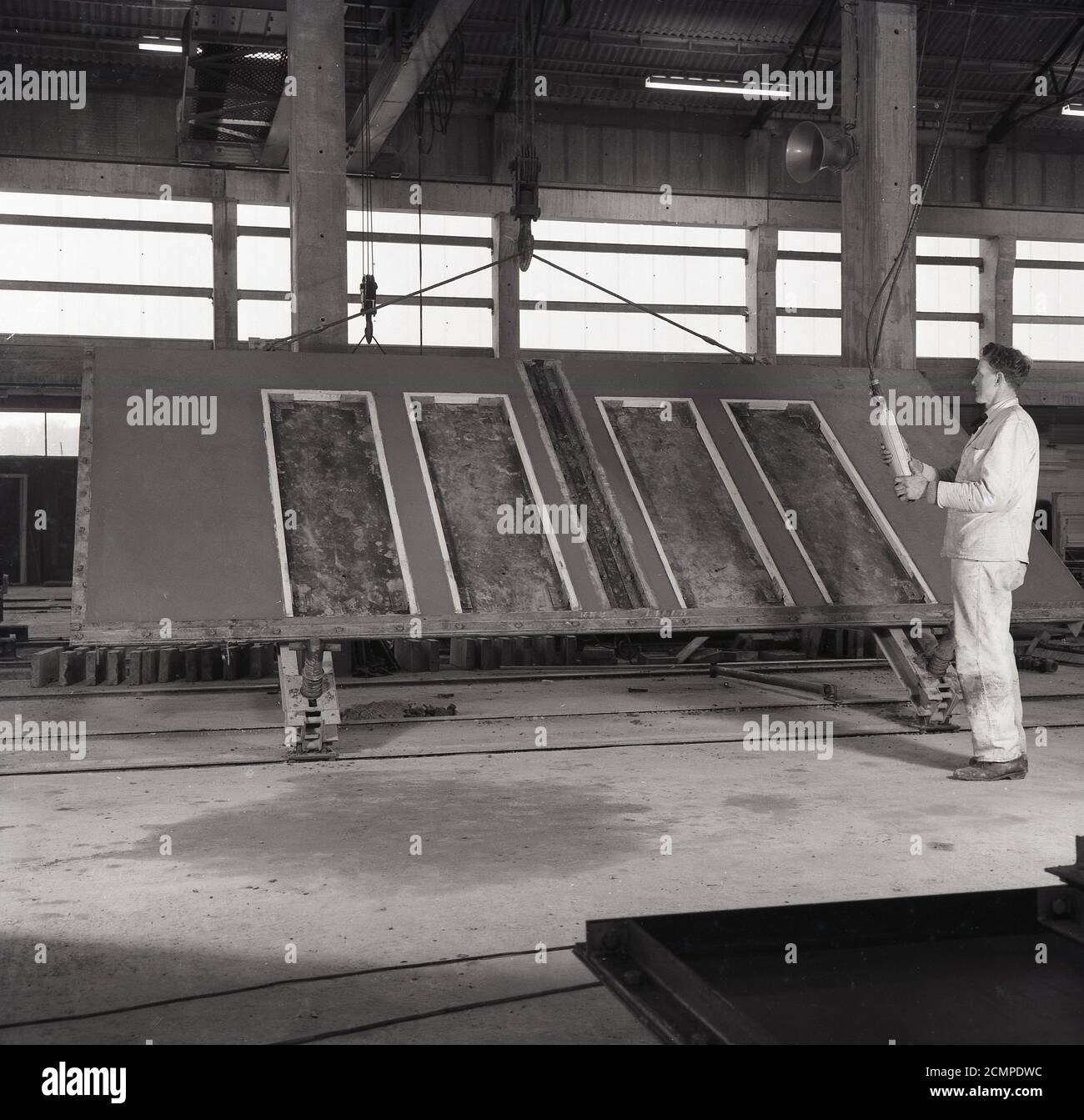 1960er Jahre, historisch, in einer Fabrik aus vorgegossenem Beton, England, Großbritannien, ein Arbeiter mit einer Betonfertigteilplatte in einer Form. In dieser Zeit gab es einen Boom in der Konstruktion von Hochhäusern und der so genannten 'brutalen' Architektur. Die Paneele wurden außerhalb des Standorts in einer kontrollierten Fabrikumgebung vorbereitet, gegossen und ausgehärtet, wodurch die Baukosten günstiger und schneller wurden, da die Kosten für qualifizierte Arbeitskräfte und Materialien vor Ort reduziert wurden. Auch da der Beton außerhalb der Baustelle hergestellt wurde, ließ er Zeit, ihn zu stärken, bevor er auf die Baustelle verlegt wurde. Stockfoto