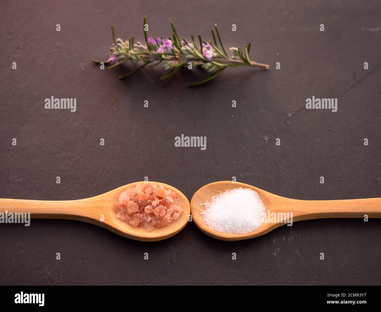 Holzlöffel mit marine Kochsalz und rosa Himalaya Salz und Rosmarin Zweig auf einer Schiefertafel Platte Stockfoto