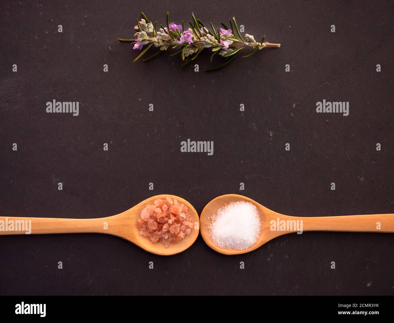 Holzlöffel mit marine Kochsalz und rosa Himalaya Salz und Rosmarin Zweig auf einer Schiefertafel Platte Stockfoto