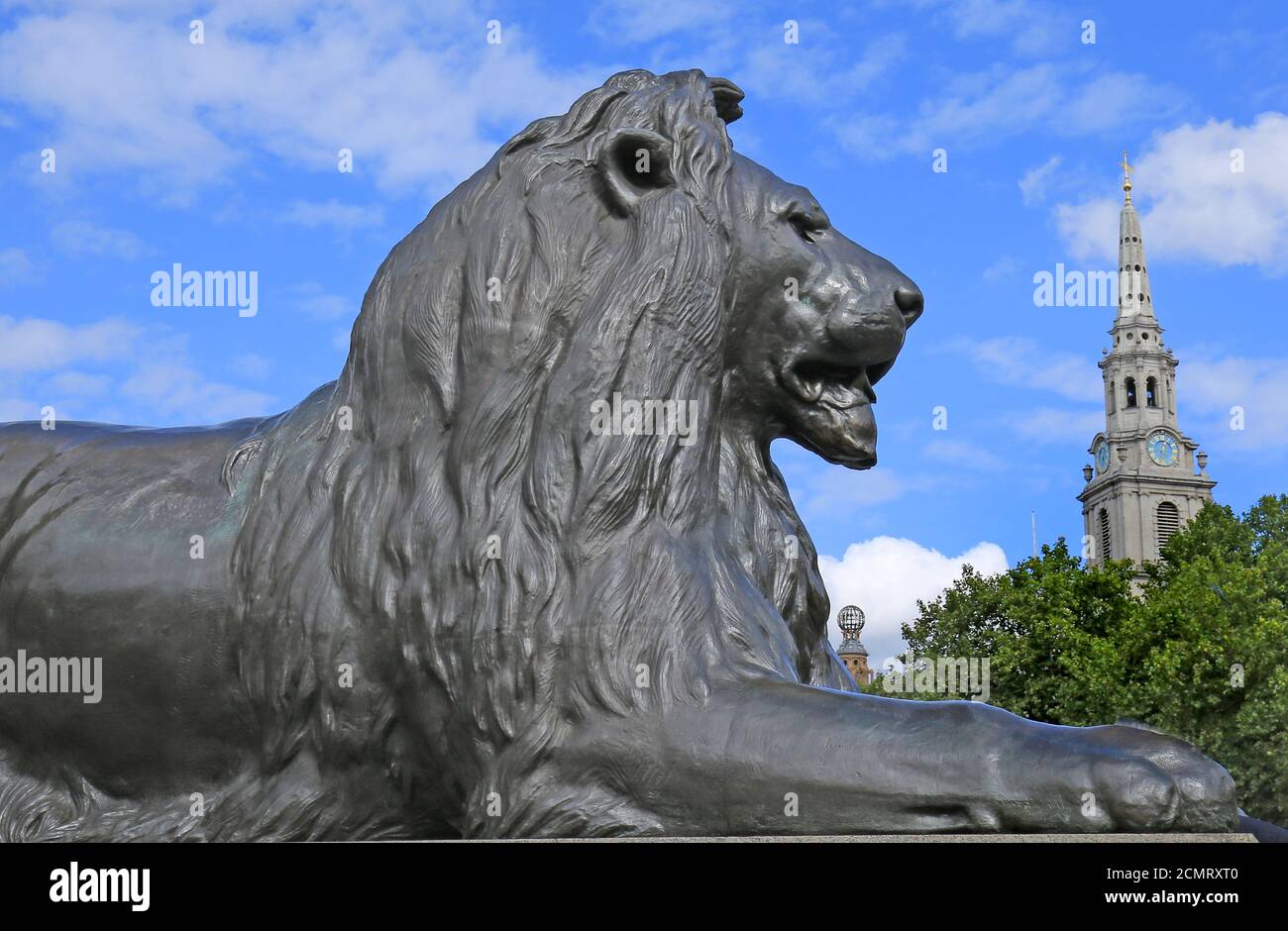 Bronze Landseer Lion Skulptur auf Trafalgar Square, mit einem schönen blau bewölkten Himmel Hintergrund, mit St. Martins im Feld Kirchturm in der Ferne Stockfoto