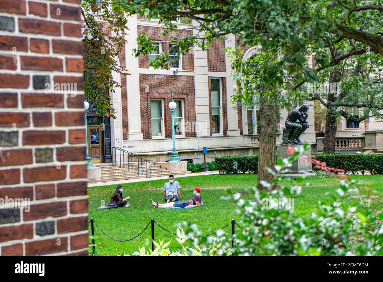 Drei Studenten mit Schutzmasken sitzen auf dem Rasen vor der Philosophy Hall, Columbia University, New York City, New York, USA Stockfoto