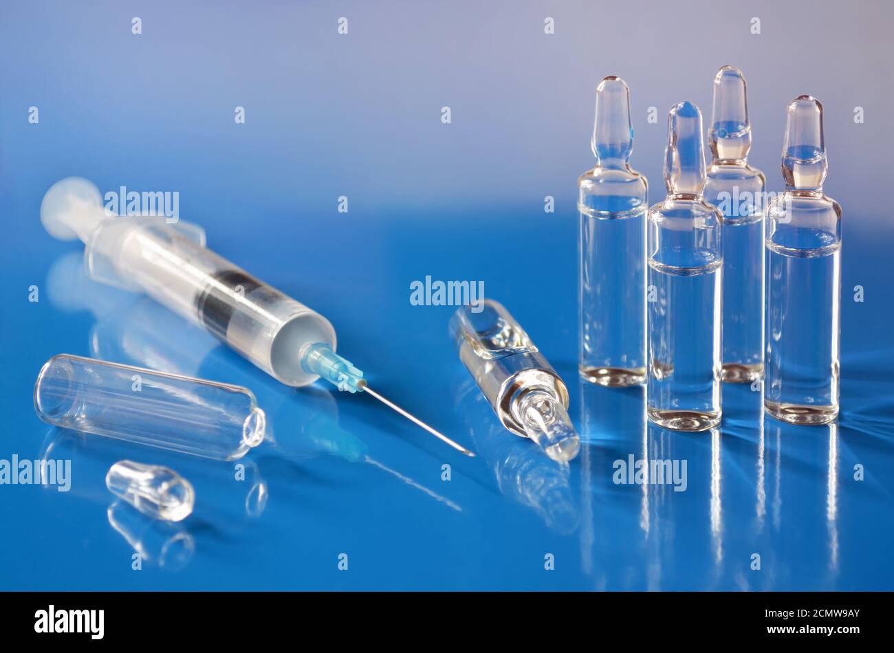 Ampullen mit Impfstoff und einer medizinischen Einwegspritze auf blauem Hintergrund in Nahaufnahme. Geringe Schärfentiefe, selektiver Fokus. Konzept der Gesundheitsversorgung. Stockfoto