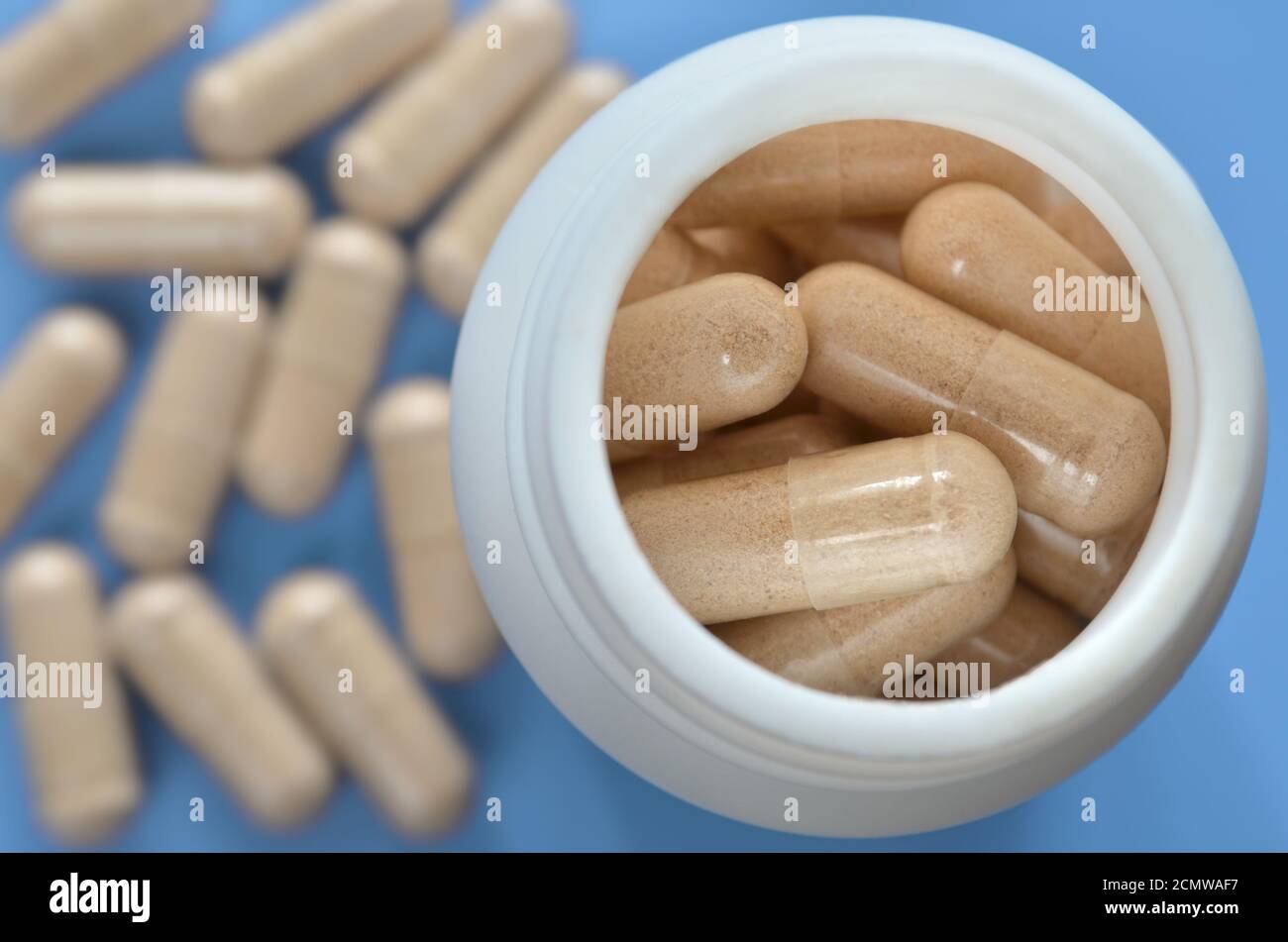 Weiße medizinische Flasche mit Pillen auf einem hellblauen defokussed Hintergrund mit verstreuten Kapseln, close-up. Gesundheitskonzept. Stockfoto