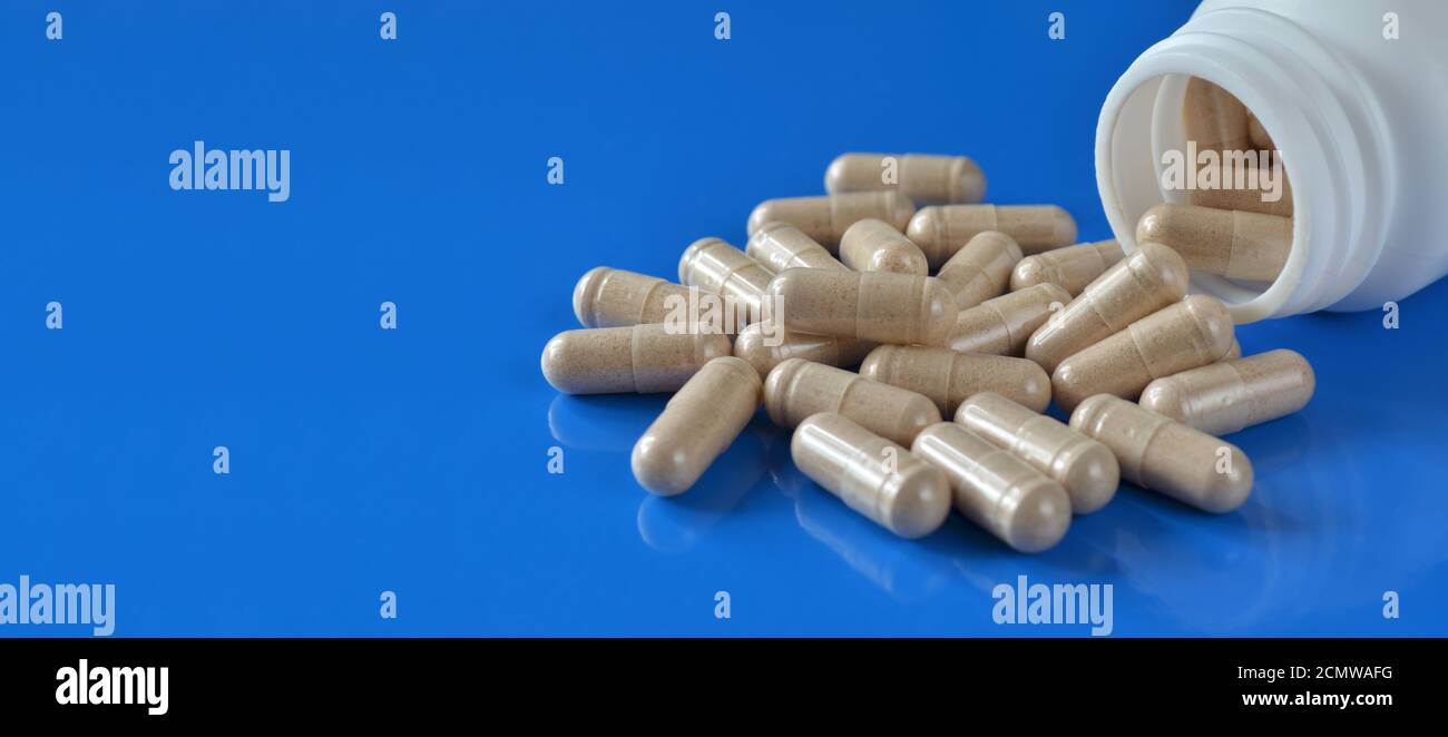 Heap Pillen-Kapseln mit einem weißen medizinischen Behälter auf einem blauen Hintergrund mit Kopierraum, selektiver Fokus. Gesundheitskonzept. Stockfoto