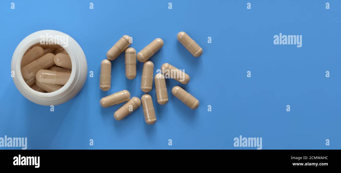 Weiße Arzneiflasche mit Droge und verstreuten Kapseln auf hellblauem Hintergrund mit Kopierraum, Draufsicht. Gesundheitskonzept. Stockfoto