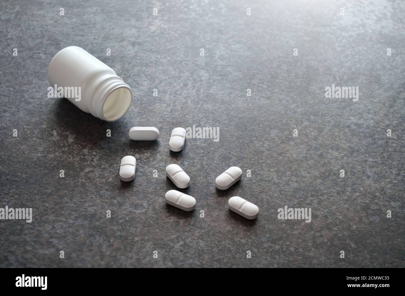 Weiße Tabletten fallen aus einer Plastikflasche auf eine dunkelgraue Tischoberfläche als Hintergrund mit Kopierraum, selektiver Fokussierung. Stockfoto